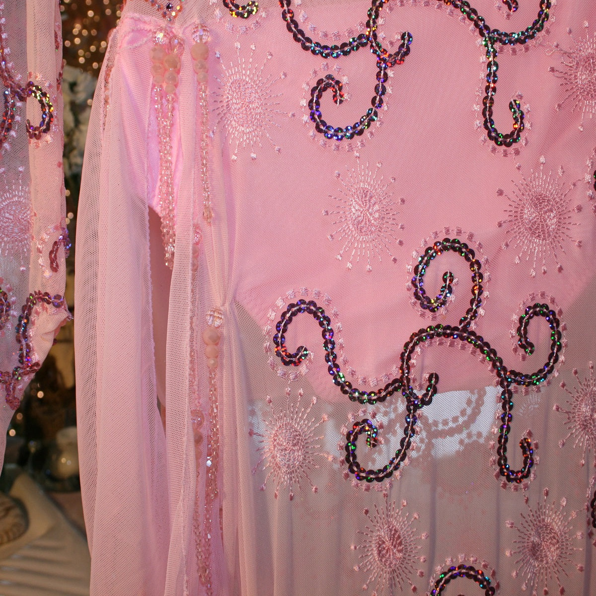 side bead details of stunning pink Latin-Rhythm dress. Its delicate soft pink stretch mesh is adorned with a mesmerizing scroll design, highlighted by two shades of glimmering pink rhinestones in a beautiful scroll design on the back, upper bodice, and left sheer side. The extensive hand beading in the skirting adds the perfect touch of elegance