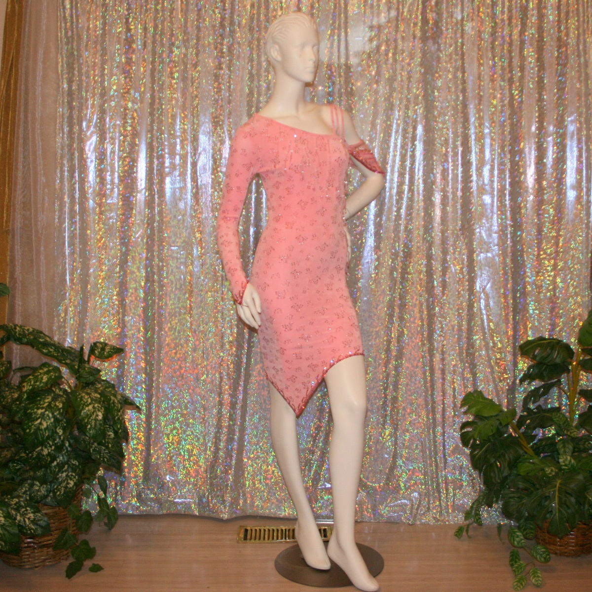 front right side view of Delicate pink Latin-rhythm dress created of light pink glitter slinky with a delicate glitter flower pattern has sleek & classic lines, long sleeve on the right side with open lattice work detailing on the left side, embellished with Swarovski rhinestone work & extensive hand beading