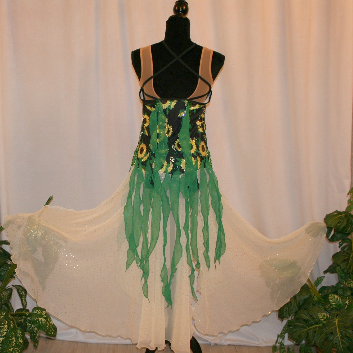 Back view of all around ballroom dress that features yards of gorgeous soft yellow champagne sequin chiffon hand cut in large petal shapes for the skirting that is short in front & cascades longer in the back. Overlays of emerald flocked green chiffon skillfully hand crafted creating thin leaf shapes. Flows so beautifully for your foxtrots & waltzes! Lots of sparkle comes from the detailed rhinestone work