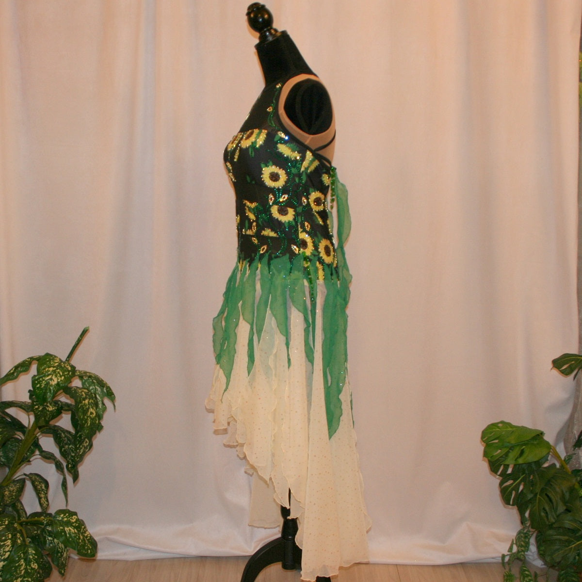 Side view of all around ballroom dress that features yards of gorgeous soft yellow champagne sequin chiffon hand cut in large petal shapes for the skirting that is short in front & cascades longer in the back. Overlays of emerald flocked green chiffon skillfully hand crafted creating thin leaf shapes. Flows so beautifully for your foxtrots & waltzes! Lots of sparkle comes from the detailed rhinestone work
