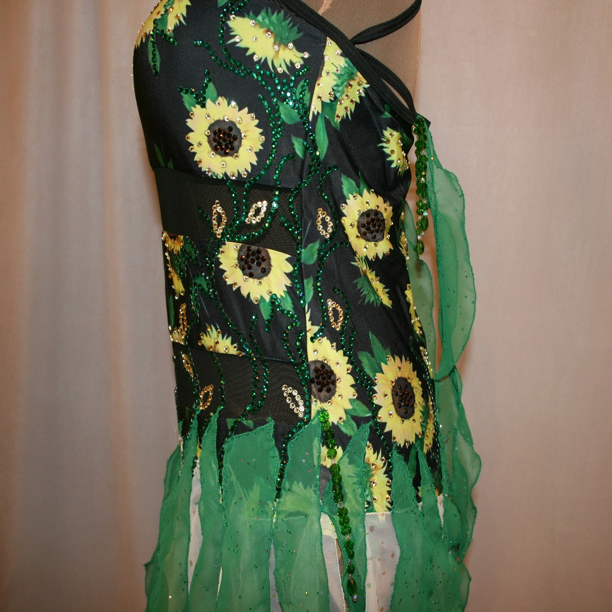 Upper side view of all around ballroom dress that features yards of gorgeous soft yellow champagne sequin chiffon hand cut in large petal shapes for the skirting that is short in front & cascades longer in the back. Overlays of emerald flocked green chiffon skillfully hand crafted creating thin leaf shapes. Flows so beautifully for your foxtrots & waltzes! Lots of sparkle comes from the detailed rhinestone work