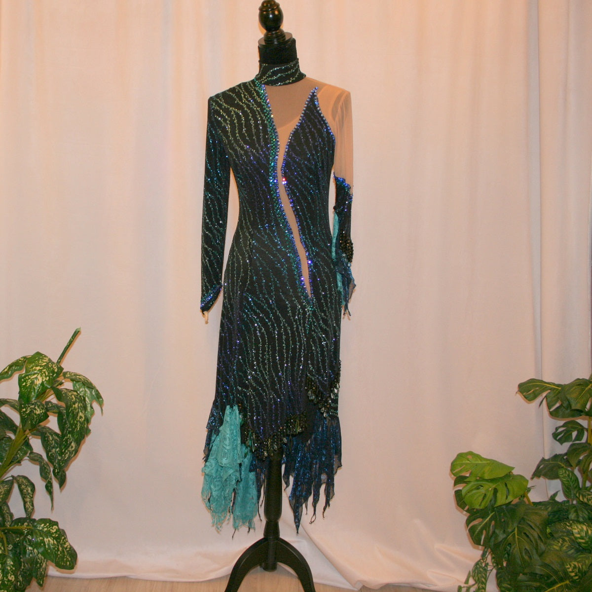 black Latin-rhythm dress sparkles plenty on the dance floor with a stunning black glitter fabric featuring a wavy turquoise, aqua & royal blue design, complete with black hand-beading, aqua teardrop shape beads, spangles, and intricate flounces in various fabrics of deep shimmering blue, turquoise, aqua & black.
