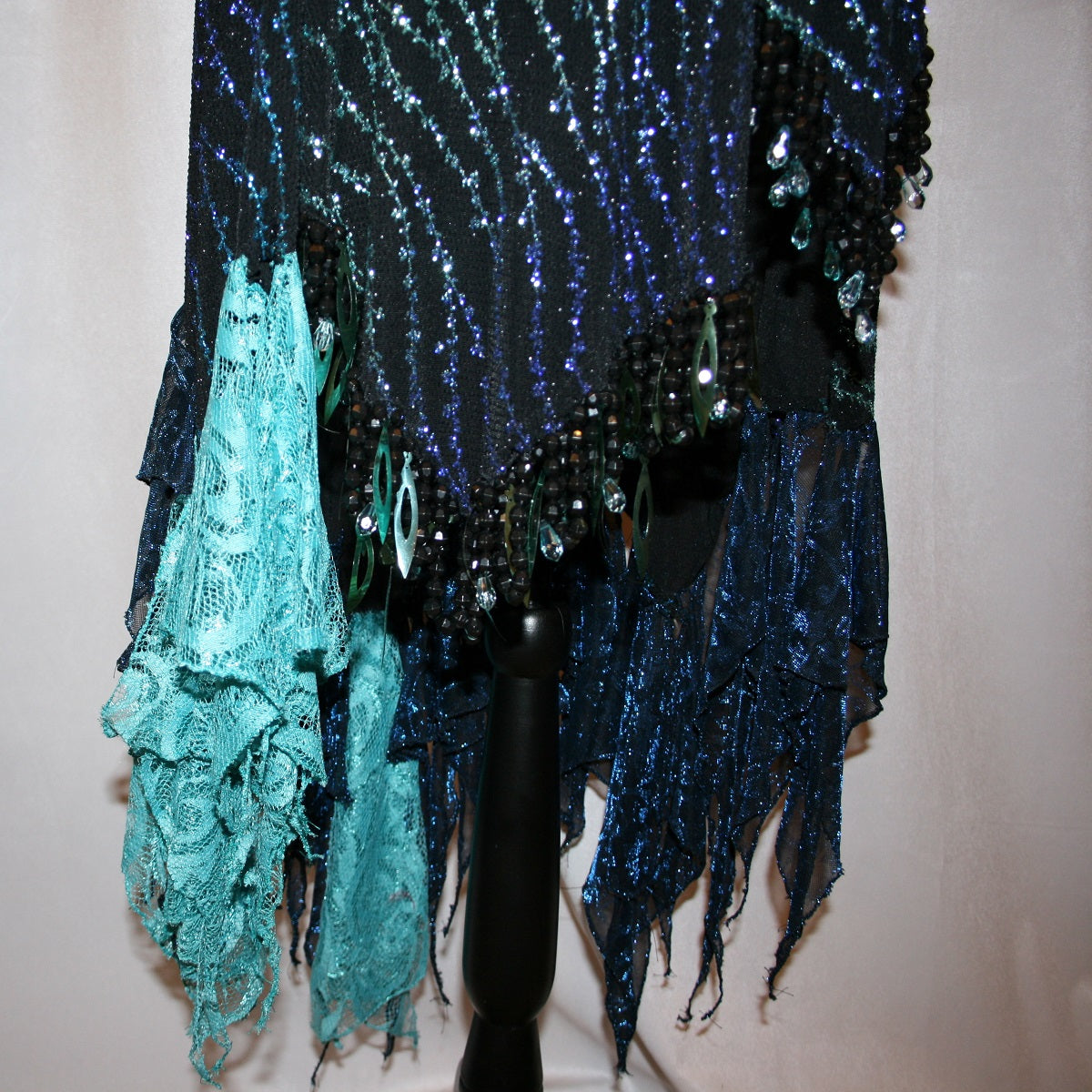 bottom details of black Latin-rhythm dress sparkles plenty on the dance floor with a stunning black glitter fabric featuring a wavy turquoise, aqua & royal blue design, complete with black hand-beading, aqua teardrop shape beads, spangles, and intricate flounces in various fabrics of deep shimmering blue, turquoise, aqua & black.
