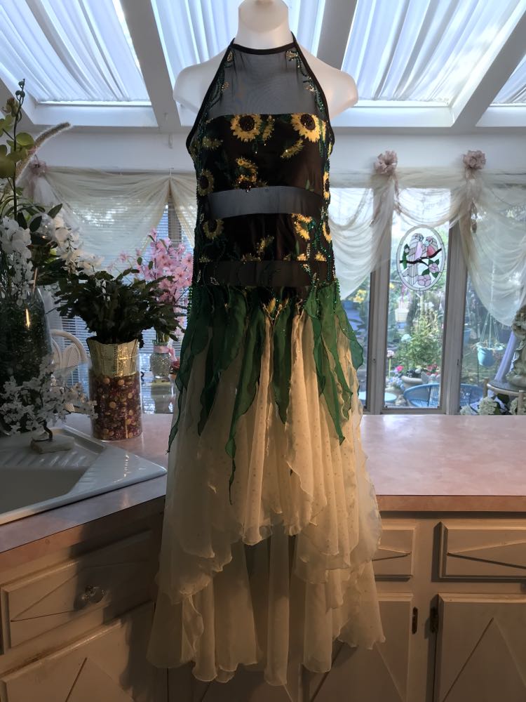 All around ballroom dress of sunflower print features yards of gorgeous soft yellow champagne sequin chiffon hand cut in large petal shapes for the skirting that is short in front & cascades longer in the back. Overlays of emerald flocked green chiffon skillfully hand crafted creating thin leaf shapes. Flows so beautifully for your foxtrots & waltzes! Lots of sparkle comes from the detailed rhinestone work