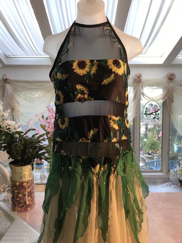 Upper close up view of all around ballroom dress features yards of gorgeous soft yellow champagne sequin chiffon hand cut in large petal shapes for the skirting that is short in front & cascades longer in the back. Overlays of emerald flocked green chiffon skillfully hand crafted creating thin leaf shapes. Flows so beautifully for your foxtrots & waltzes! Lots of sparkle comes from the detailed rhinestone work