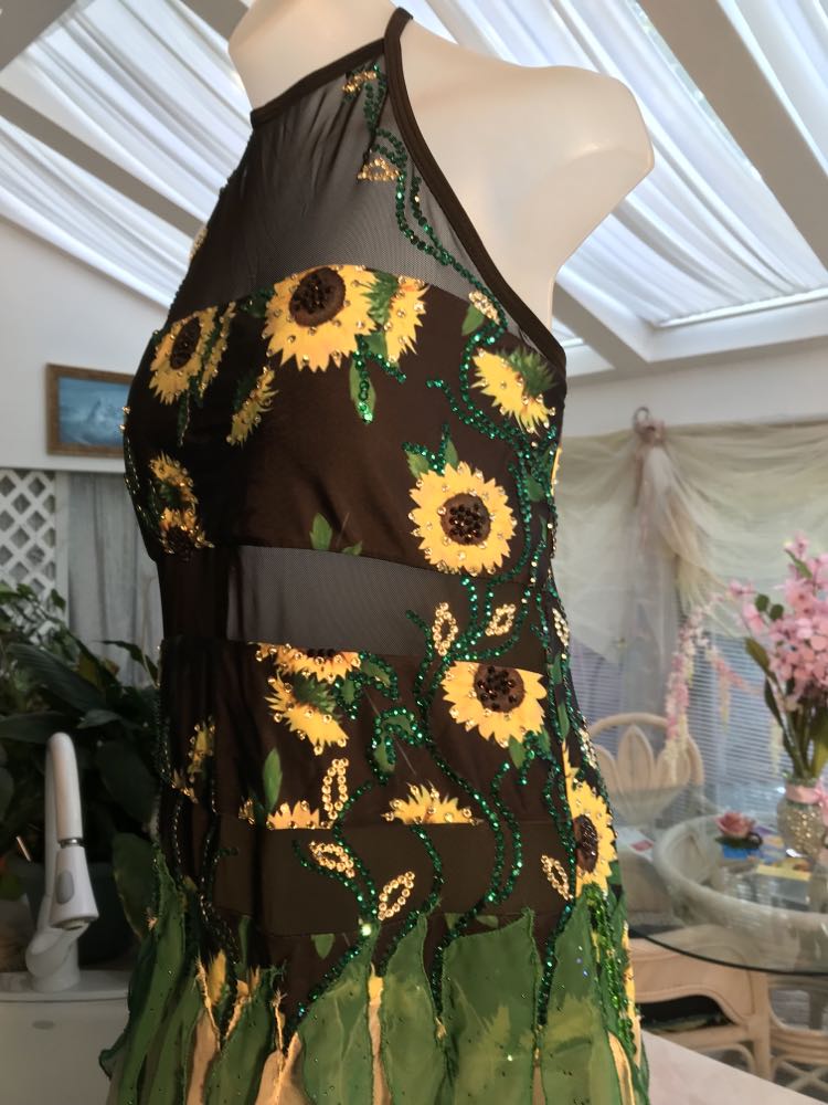 Close side view of all around ballroom dress features yards of gorgeous soft yellow champagne sequin chiffon hand cut in large petal shapes for the skirting that is short in front & cascades longer in the back. Overlays of emerald flocked green chiffon skillfully hand crafted creating thin leaf shapes. Flows so beautifully for your foxtrots & waltzes! Lots of sparkle comes from the detailed rhinestone work