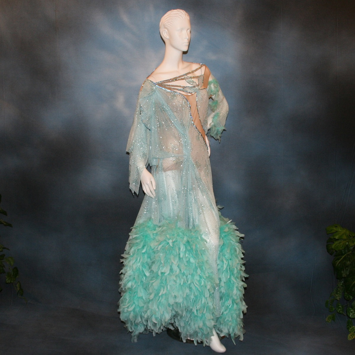 Crystal's Creations Aqua blue ballroom dress created in gorgeous aqua blue glitter sheer mesh overlaid on a nude illusion base has lots of gorgeous aqua chandelle feathers, embellished with aquamarine Swarovski rhinestone work. This ballroom dress also features delicate Swarovski embellished strap detailing.