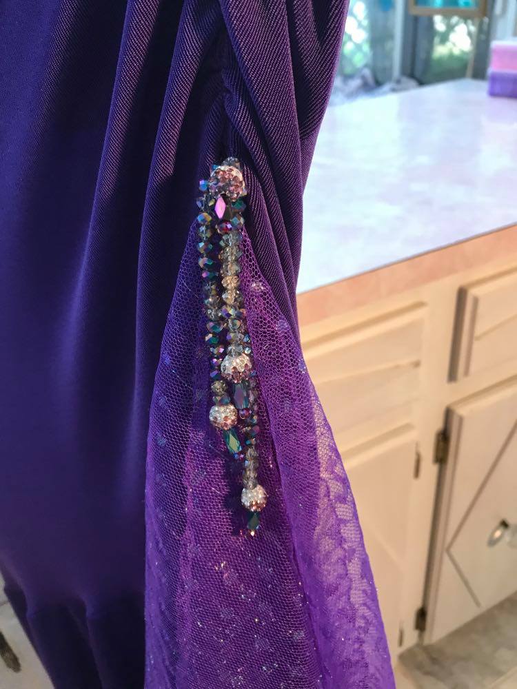 Lower detail of Crystal's Creations Purple Latin/rhythm/tango dress created of deep grape purple solid slinky with a touch of Swarovski rhinestone work done in metallic light gold & deep velvet purple, along with some hand beading & some gorgeous glittery floats.