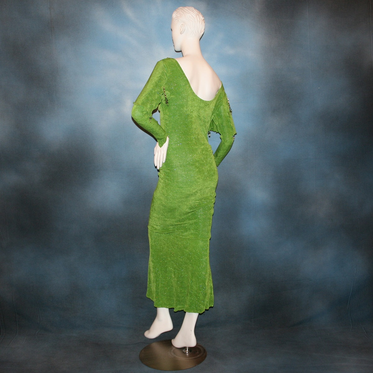 bach view of Apple green social Latin/rhythm dress was created of apple green glitter slinky, features ruching on the right side, long sleeves, scoop back, & full skirting with open side that has Swarovski hand beaded detail