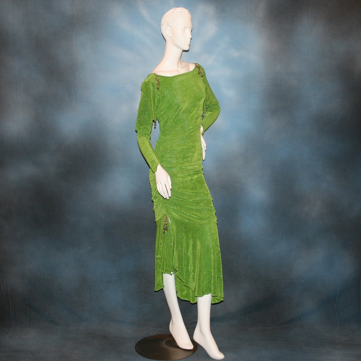 side view of Apple green social Latin/rhythm dress was created of apple green glitter slinky, features ruching on the right side, long sleeves, scoop back, & full skirting with open side that has Swarovski hand beaded detail