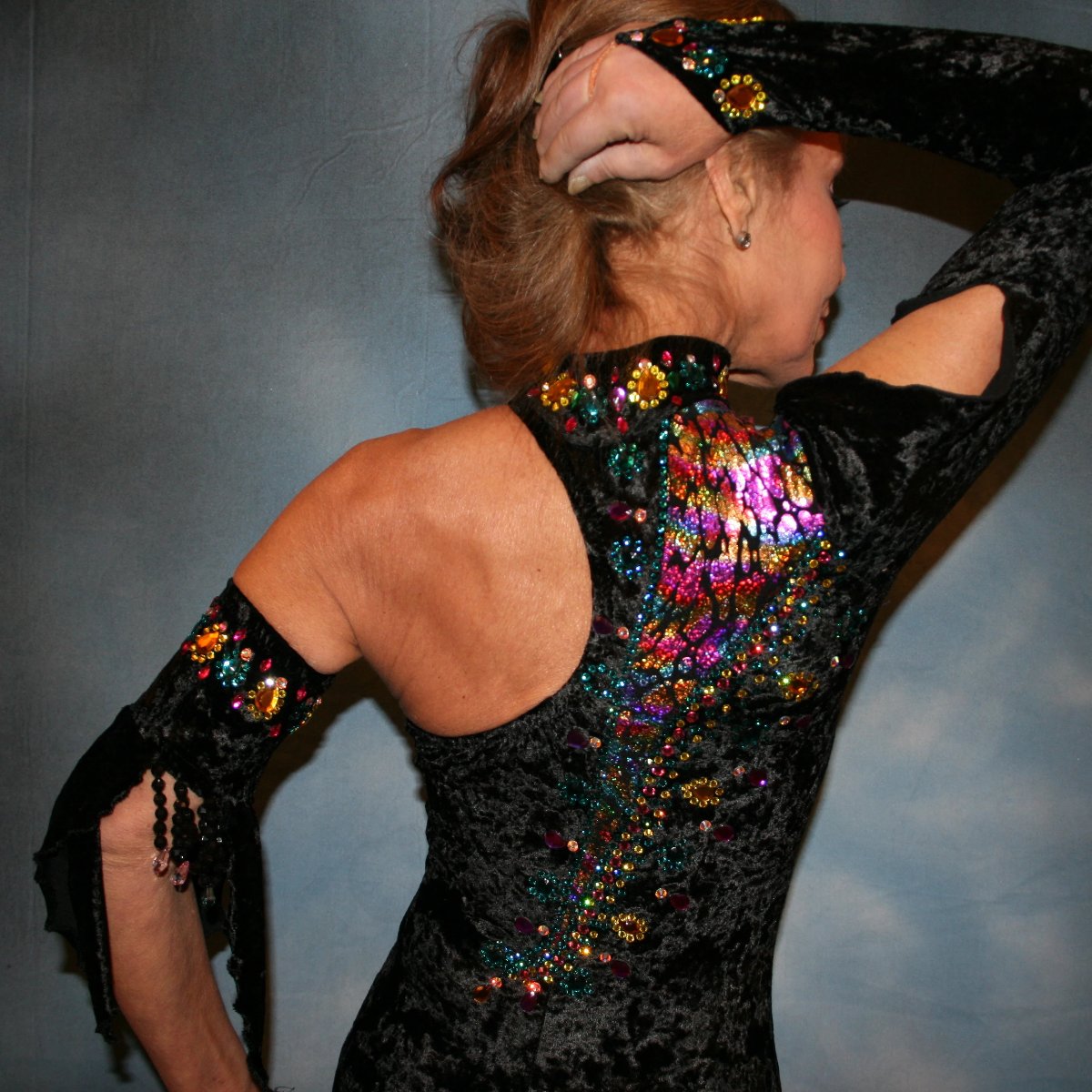 close upper back view of Black Latin/rhythm dress created in black panne velvet with colorful confetti hologram lycra accents, is embellished with hand beading, Swarovski CAB, citrine, & blue zircon rhinestones plus large colorful acrylic gems.