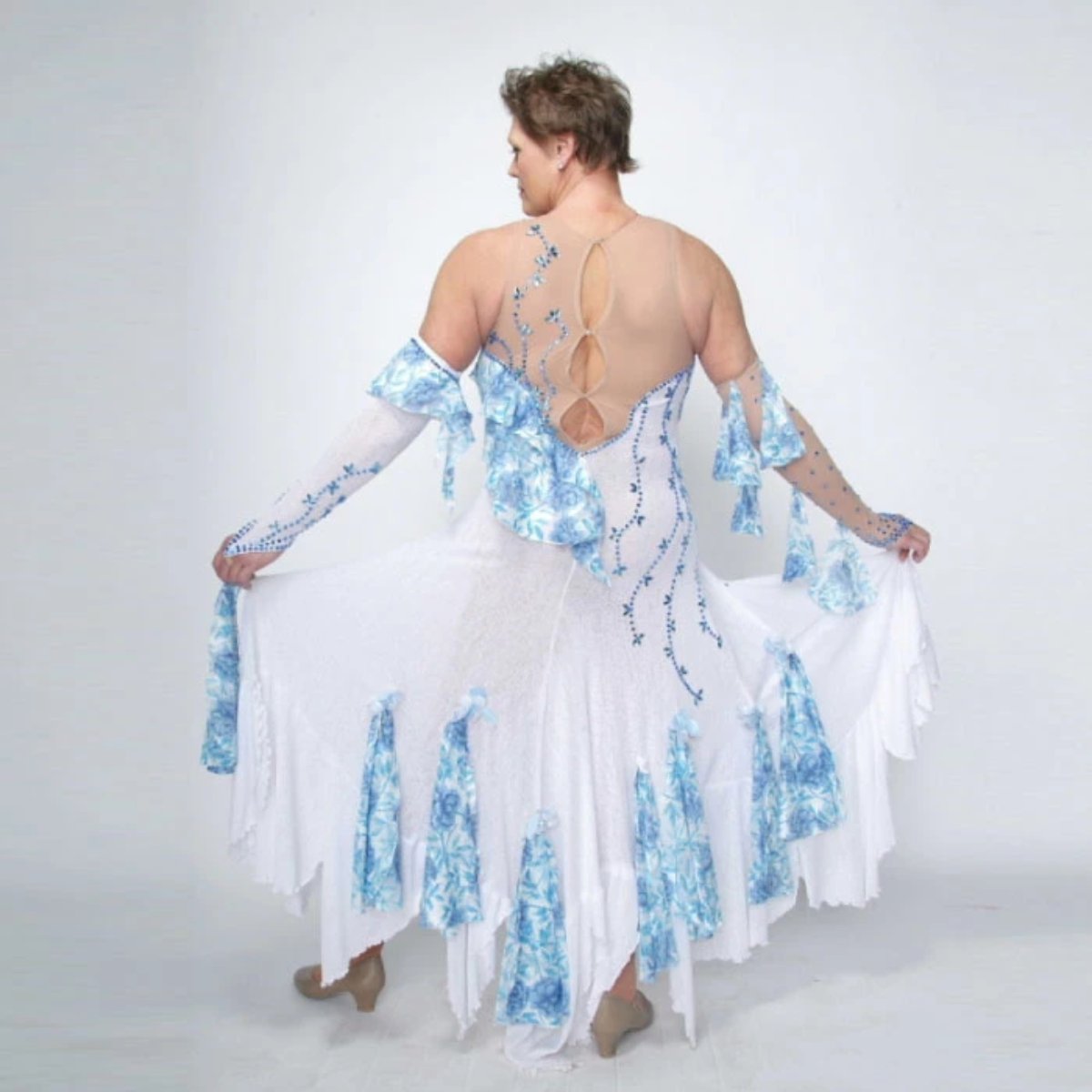 back view of White ballroom dress with blue accents was created on nude illusion of a soft white knit with flounce accents of sky blue & white floral print satin, embellished with sapphire Swarovski stonework & miniature white silk roses.