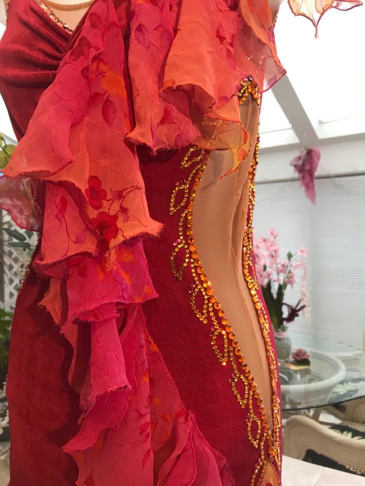 left close up view of Gorgeous rose colored converta ballroom dance dress was created on a nude illusion base of rose colored slinky with flounces of a gorgeous oriental flower print crinkle chiffon of pinks, yellows & oranges. Detailed Swarovski rhinestone work which ties in so beautifully with with the print chiffon, is done in pinks, yellows & orange.