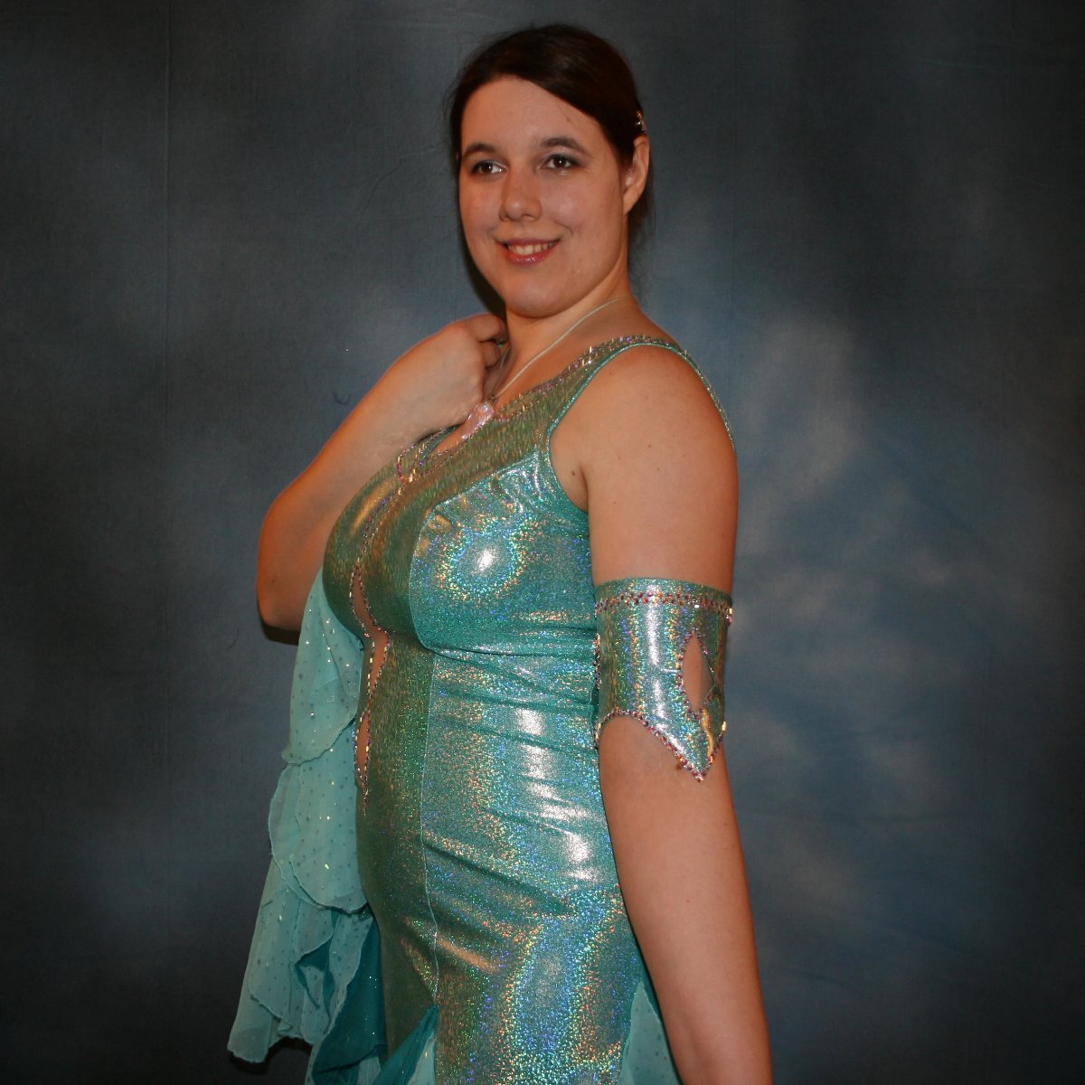 Crystal's Creations close up side view of Aqua Latin/rhythm dress created of gorgeous hologram base with flounces of aqua champagne sequin chiffon & teal glitter chiffon, embellished with CAB Swarovski stone work, with strap detailing on back. I envision this magical dress a gorgeous rumba, bolero or even a great solo dress for a waltz or foxtrot….or for an all around division.
