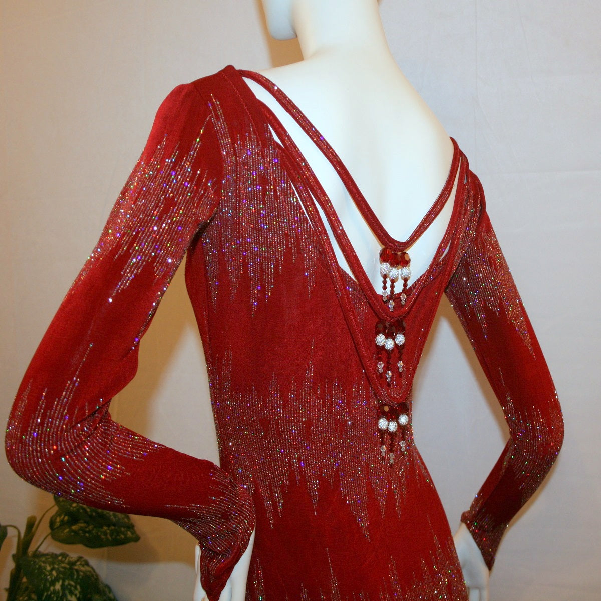 upper back view of Deep scarlette red Latin-rhythm-tango dress created in scarlette red glitter slinky with an awesome electrifying silver AB glitter pattern, features draping straps with Swarovski hand beading detailing on the back, long sleeves with a double split skirting at bottom.
