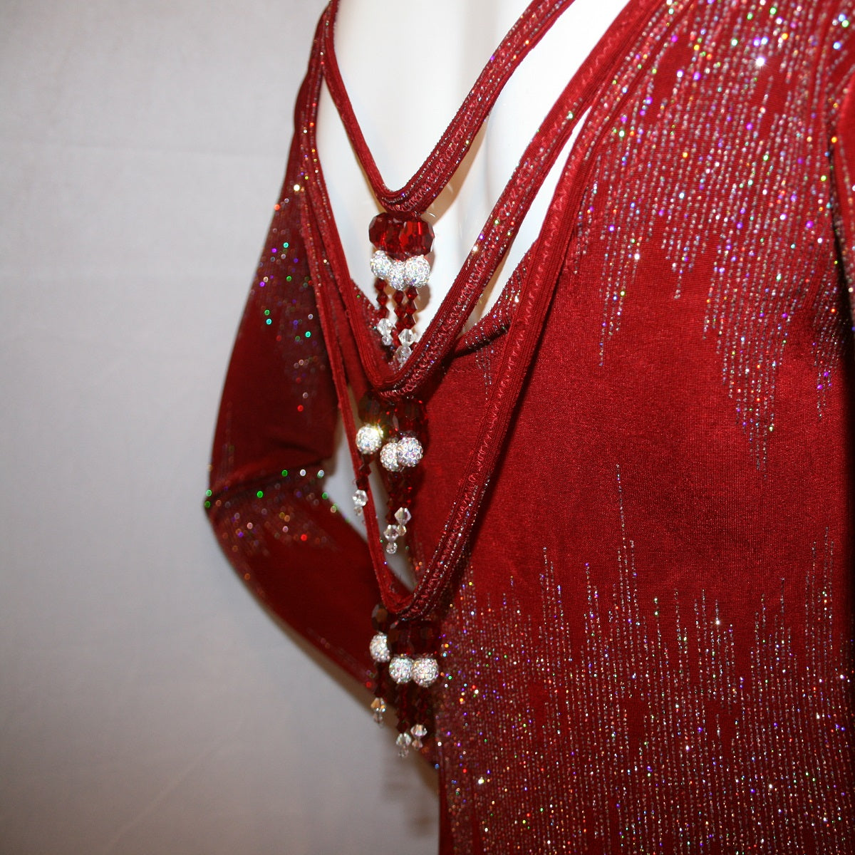 close view of bead details of Deep scarlette red Latin-rhythm-tango dress created in scarlette red glitter slinky with an awesome electrifying silver AB glitter pattern, features draping straps with Swarovski hand beading detailing on the back, long sleeves with a double split skirting at bottom.