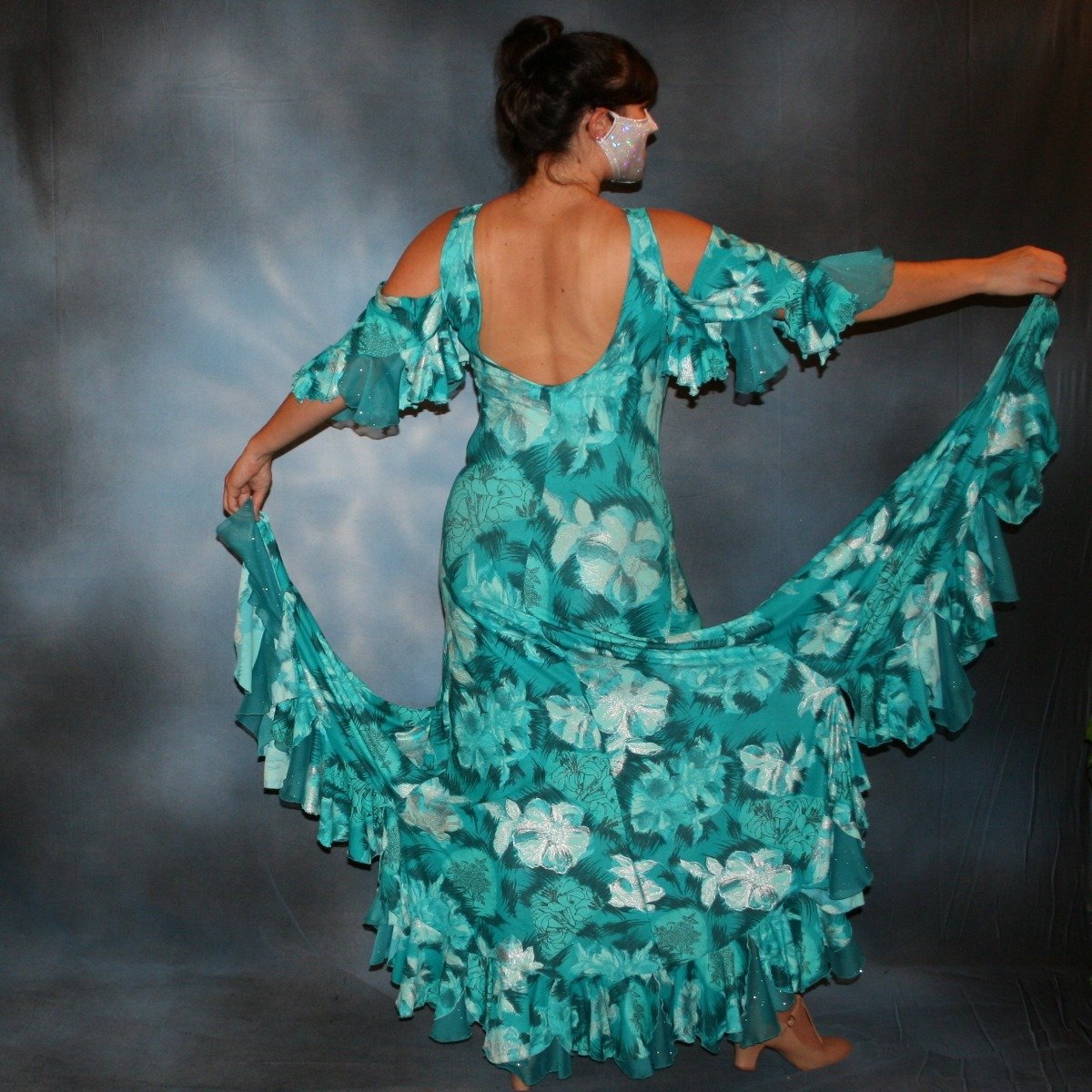 Crystal's Creations back view of Gorgeous teal tropical print social ballroom dress created in tropical lycra print in shades of teal with a bit of silver sheen accents...absolutely gorgeous fabric! This social ballroom dress features very full skirting with 2 slits & oodles of flounces of the same teal tropical print lycra with intermittent flounces of teal glitter chiffon...along with draping, cold shoulder flounce sleeves...and a low back