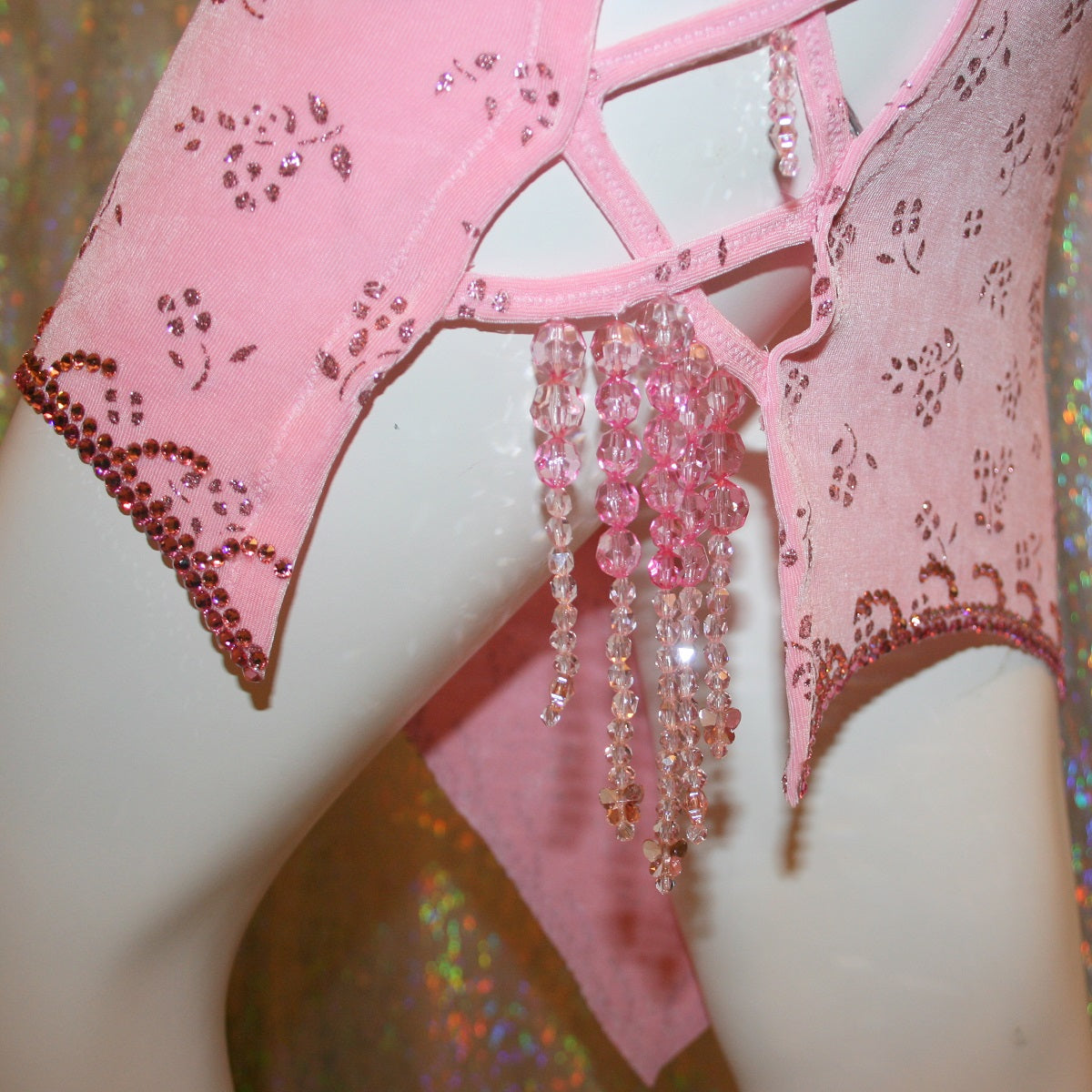 close view of details on Delicate pink Latin-rhythm dress created of light pink glitter slinky with a delicate glitter flower pattern has sleek & classic lines, long sleeve on the right side with open lattice work detailing on the left side, embellished with Swarovski rhinestone work & hand beading