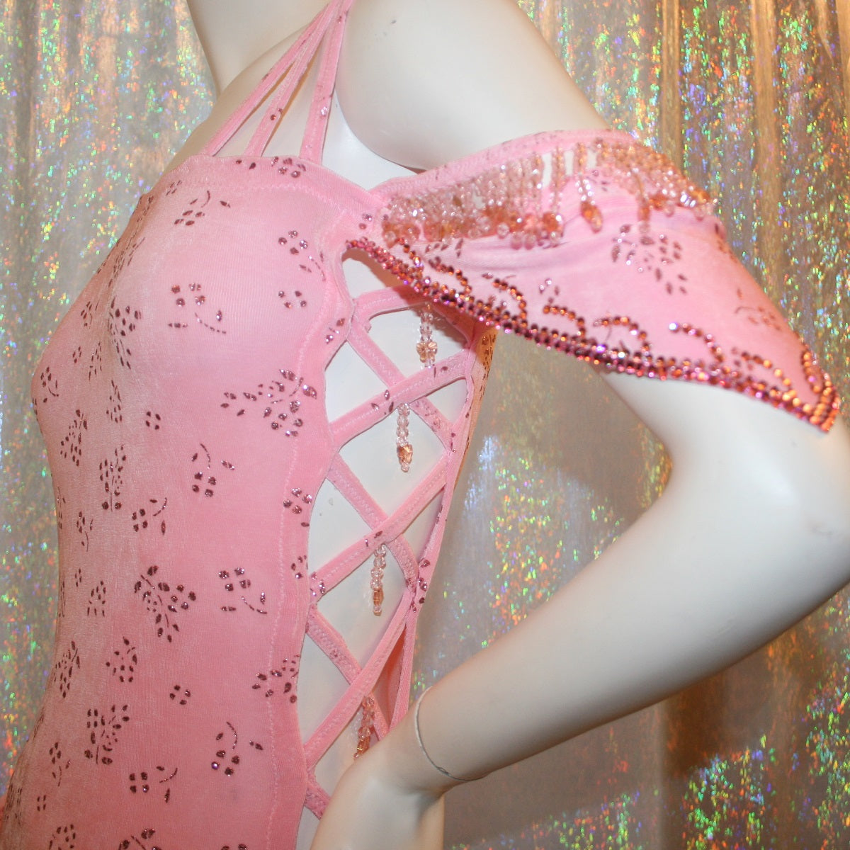 top left view of Delicate pink Latin-rhythm dress created of light pink glitter slinky with a delicate glitter flower pattern has sleek & classic lines, long sleeve on the right side with open lattice work detailing on the left side, embellished with Swarovski rhinestone work & hand beading