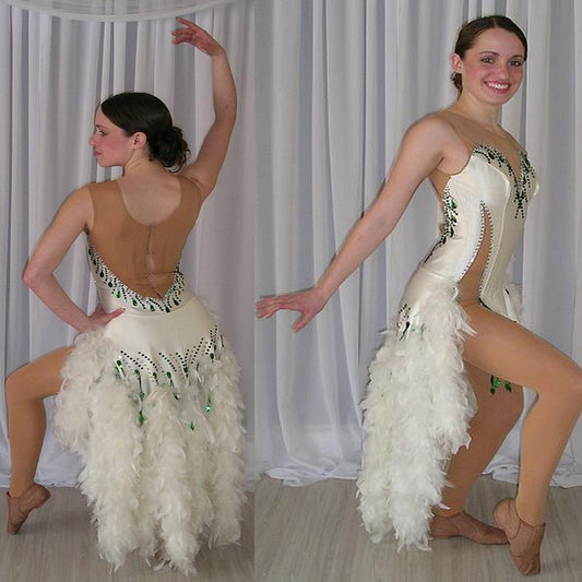 White Latin/rhythm dress created of white heavy lycra on a nude illusion base with white chandelle feathers & embellished with crystal and emerald green Swarovski rhinestone work.