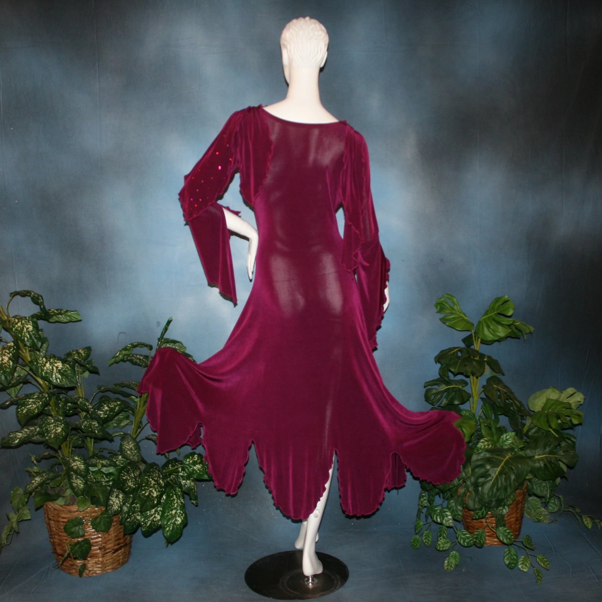 back view of Magenta social ballroom dress created in luxurious solid slinky fabric with cutouts at bustline & attached double draping on shoulders, embellished with magenta Swarovski rhinestones, features a scalloped skirt edge. Very full around bottom & can be a beginner ballroom dancer smooth ballroom show or competition dress.