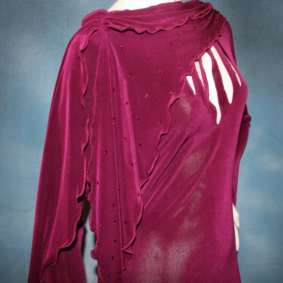 close side view of Magenta social ballroom dress created in luxurious solid slinky fabric with cutouts at bustline & attached double draping on shoulders, embellished with magenta Swarovski rhinestones, features a scalloped skirt edge. Very full around bottom & can be a beginner ballroom dancer smooth ballroom show or competition dress.
