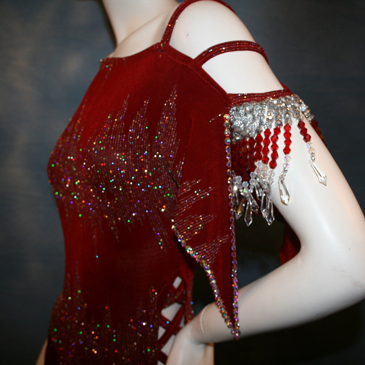 close top detail view of Deep scarlette red Latin rhythm dress created in glitter slinky with an awesome electrifying glitter pattern features lattice detailing in the sides, one long sleeve & interesting detailing on the opposite shoulder with Swarovski hand beading & Crystal Ab rhinestone work edging the skirting, split cape sleeve & long sleeve.
