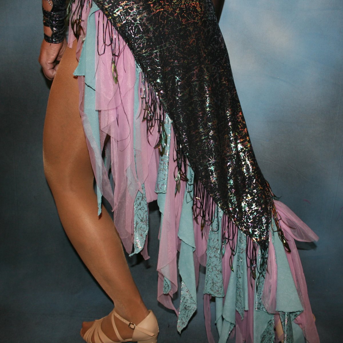 Crystal's Creations close lower view of Striking iridescent black Latin/rhythm dress of iridescent splash lycra fabric has tones of aqua and orchid throughout. The angle style skirt has wispy founces of aqua and orchid chiffon and drips with hand beading and aqua bangles. It also features sexy strap detailing down one arm, in open torso area and back. The other sheer sleeve is topped with a cap of hand beading and bangles.