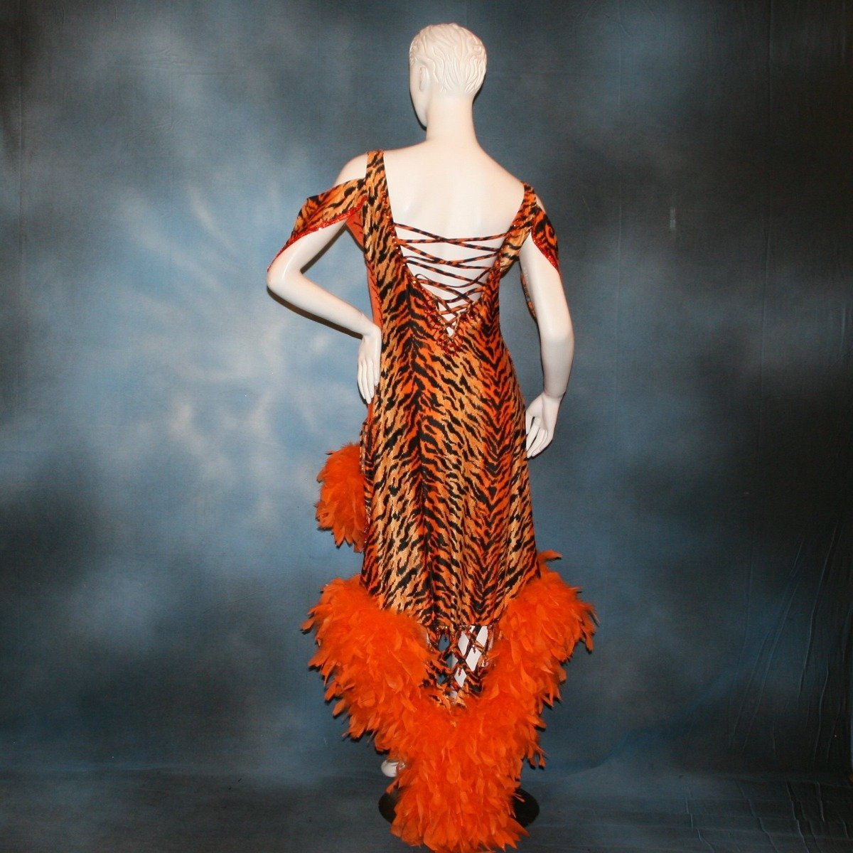 back view of Crystal's Creations Tiger print & orange Latin/rhythm dress created of tiger print lycra & luxurious orange solid slinky has color blocking, lattice work detailing in front bodice, split sides & low back, as well as intriguing longer back skirting, adorned with orange chandelle feathers, also features detailed Swarovski rhinestone work!