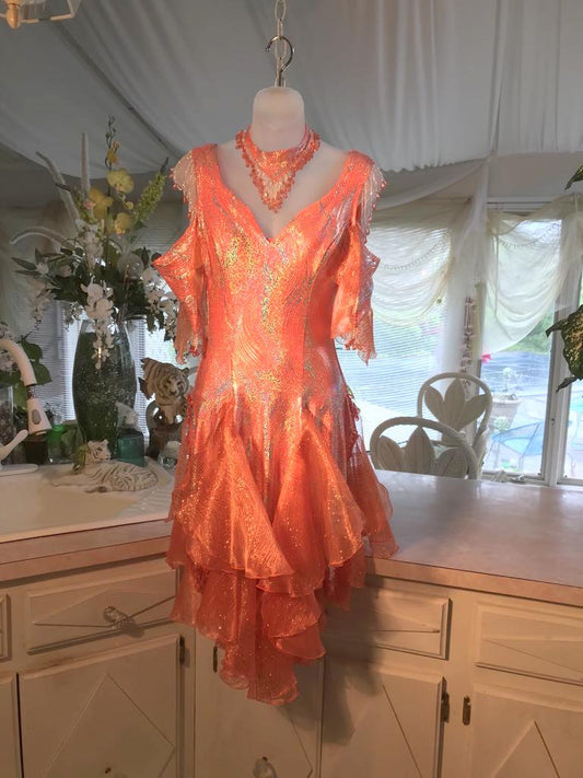 With added arm embellishments & more hand beading, Crystal's Creations Orange Latin/rhythm dress was created in orange & silver metallic print lycra with oodles of glitter organza flounces & accents, has back strap detailing, embellished with extensive Swarovski hand beading & has matching Swarovski hand beaded neckpiece.