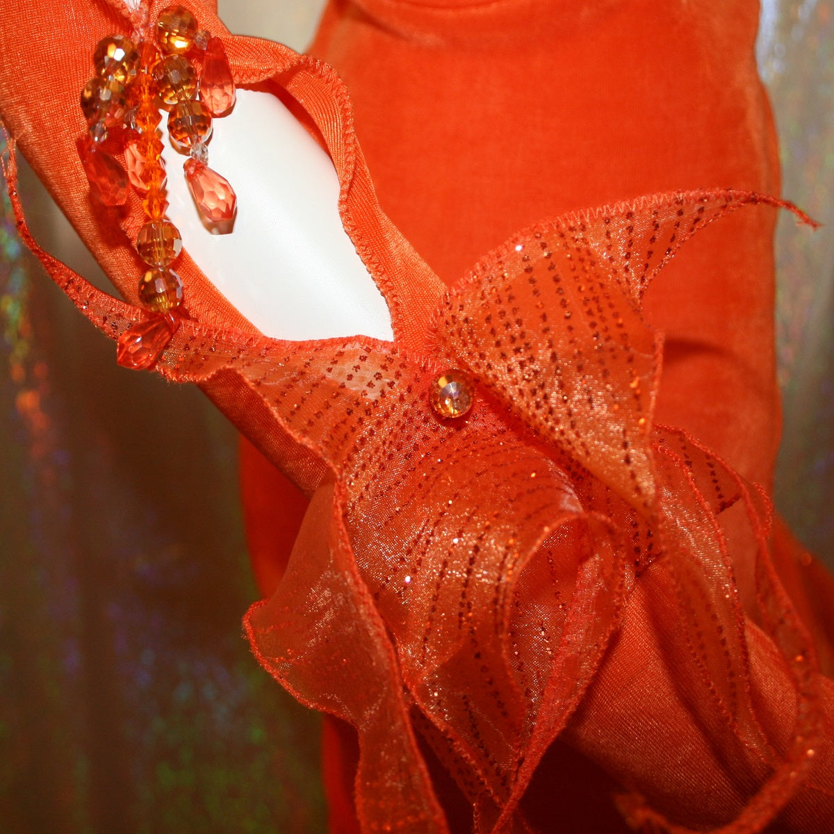 Crystal's Creations close up right wrist view of Orange Latin/rhythm dress was created in luxurious orange solid slinky with oodles of glitter organza flounces & accents, embellished with a touch of Swarovski hand beading.