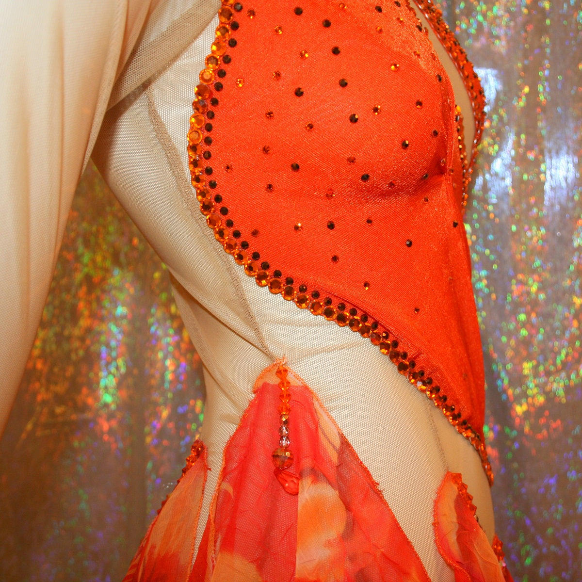 close right side view of Orange Latin-rhythm dress created on a nude illusion base of luxurious orange solid slinky with orange tropical print chiffon skirting is embellished with orange & bronze Swarovski rhinestone work & hand beading.