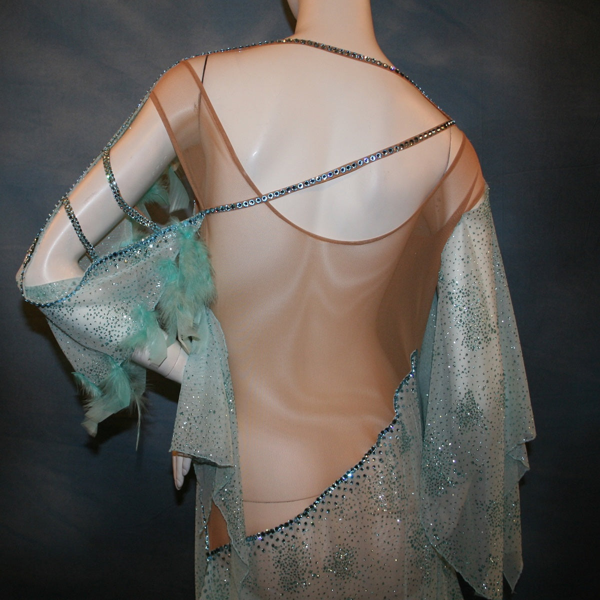 Crystal's Creations back detail view of Aqua blue ballroom dress created in gorgeous aqua blue glitter sheer mesh overlaid on a nude illusion base has lots of gorgeous aqua chandelle feathers, embellished with aquamarine Swarovski rhinestone work. This ballroom dress also features delicate Swarovski embellished strap detailing.