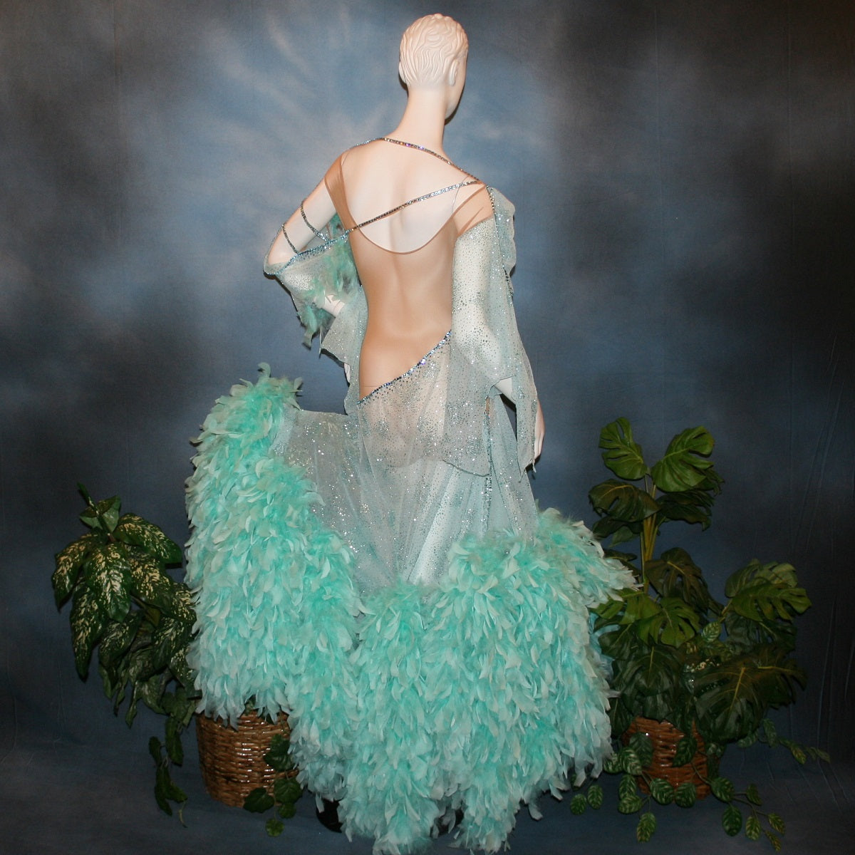 Crystal's Creations back view of Aqua blue ballroom dress created in gorgeous aqua blue glitter sheer mesh overlaid on a nude illusion base has lots of gorgeous aqua chandelle feathers, embellished with aquamarine Swarovski rhinestone work. This ballroom dress also features delicate Swarovski embellished strap detailing.