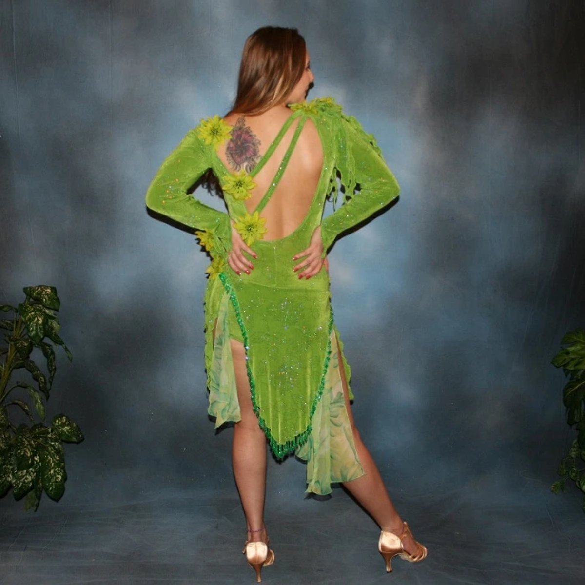 back view of Green Latin/rhythm dress created in apple green glitter slinky fabric, with print chiffon accents, embellishing done of silk flowers with Swarovski rhinestone work, also features back strap detailing along with extensive hand beading on skirt edges & choker.