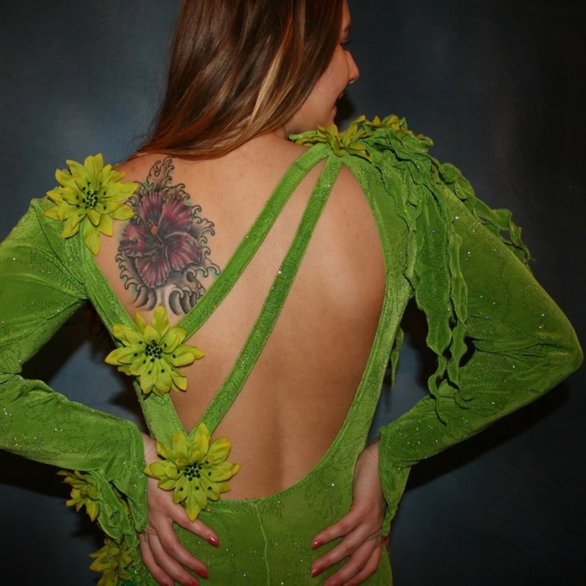close upper back view of Green Latin/rhythm dress created in apple green glitter slinky fabric, with print chiffon accents, embellishing done of silk flowers with Swarovski rhinestone work, also features back strap detailing along with extensive hand beading on skirt edges & choker.