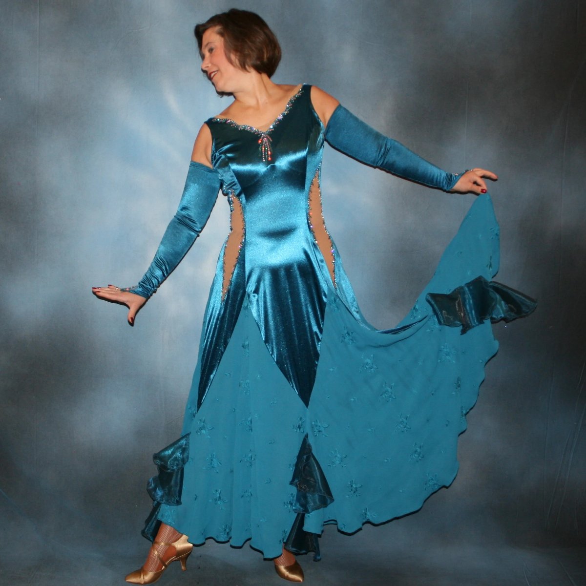 Crystal's Creations Blue ballroom dance dress was created in luxurious deep sea blue stretch satin with deep sea blue crepe chiffon embroidered insets, organza flounces…nude illusion cutout detailing…embellished with CAB & blue zircon Ab Swarovski stonework.