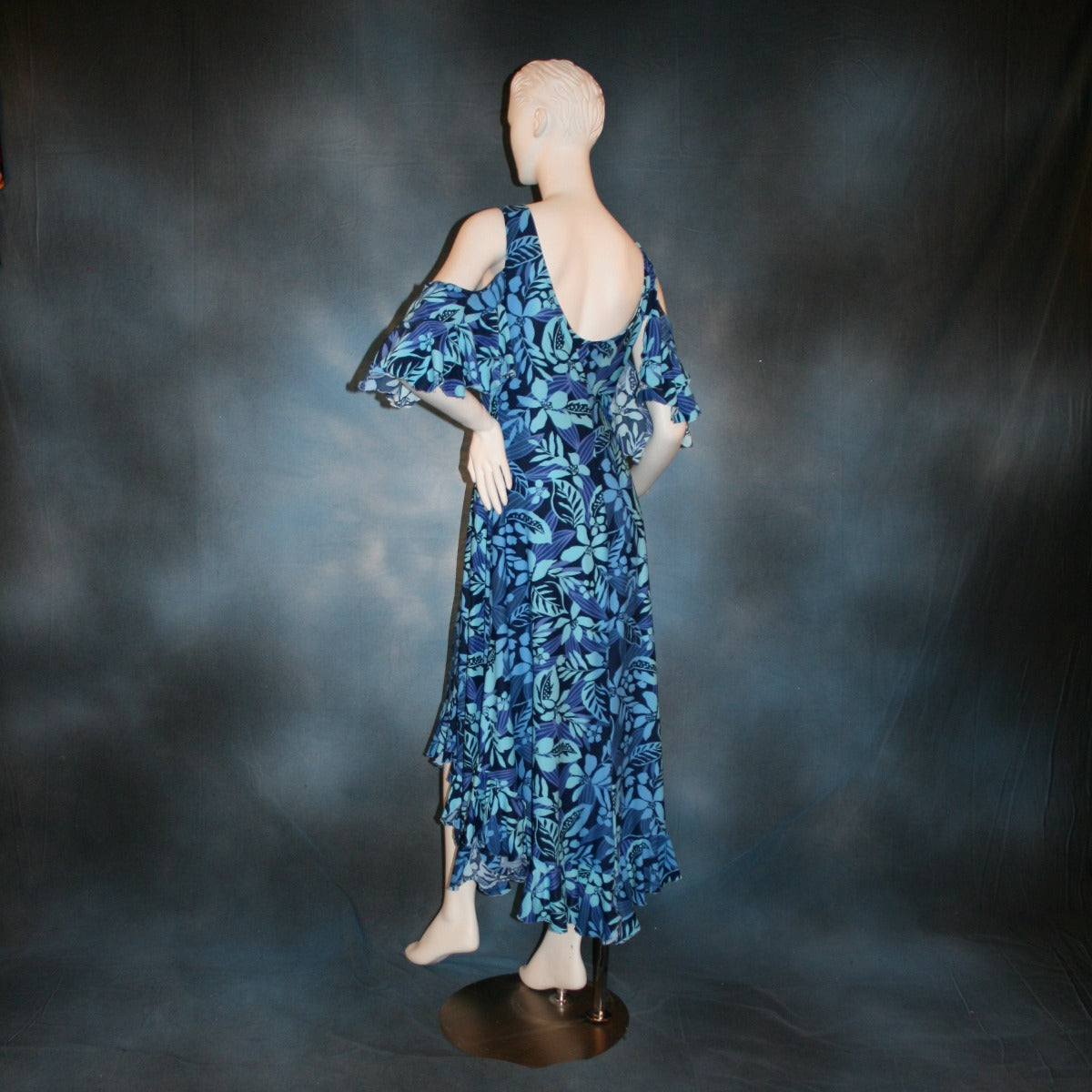 back view of Blue social ballroom dress created in tropical blue print lycra with oodles of flounces, draping cold shoulder sleeves with flounces.