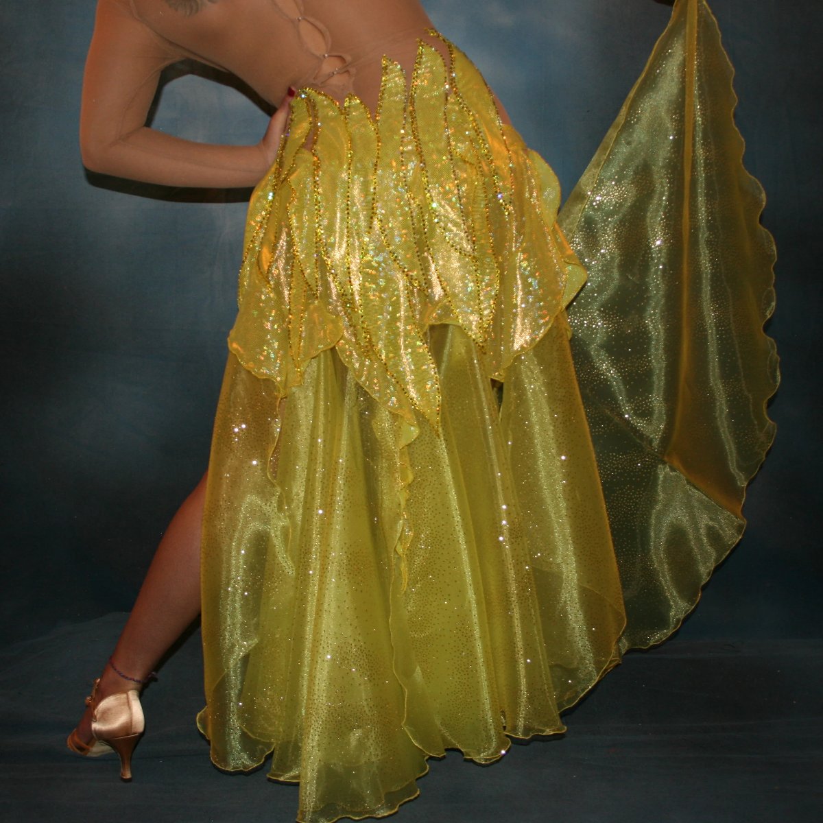 Crystal's Creations close up bottom back view of Yellow Latin/rhythm dress created of yellow hologram lycra, with handcut petal appliques overlaid artistically on nude illusion base,embellished with citrine & jonquil ab Swarovski rhinestones, with converta skirt of yards of glittered organza.