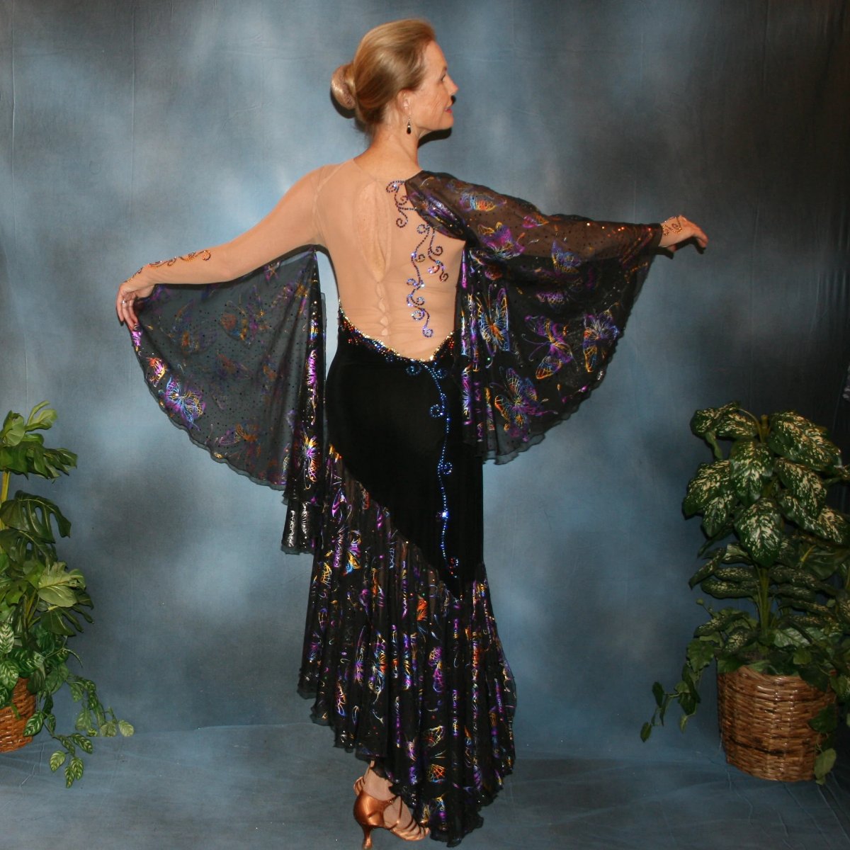 back view of Black tango dress created of black luxurious solid slinky artistically patterned out on a nude illusion base, this dramatic dress design features hologram butterfly print flounces & floats. Crystal Meridian Blue Swarovski rhinestones embellish in detail to finish.