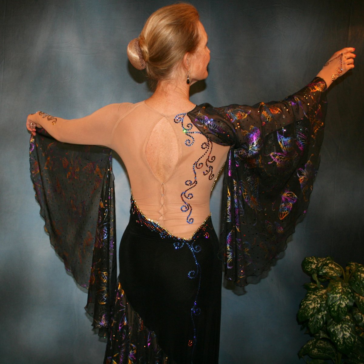 upper back view of Black tango dress created of black luxurious solid slinky artistically patterned out on a nude illusion base, this dramatic dress design features hologram butterfly print flounces & floats. Crystal Meridian Blue Swarovski rhinestones embellish in detail to finish.