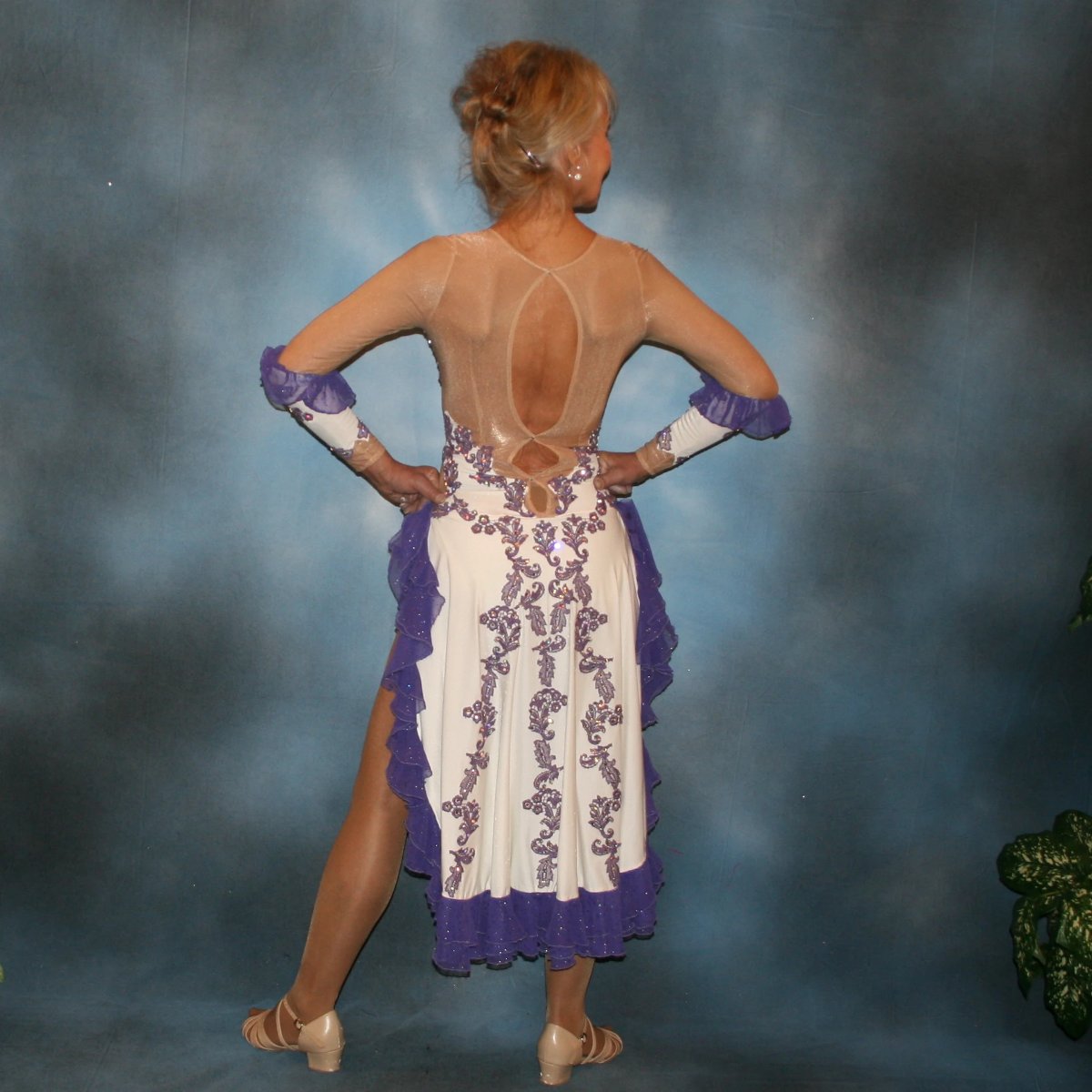 back view of White Latin/rhythm dress created with purple lace motifs embellished with crystal Aurora borealis Swarovski rhinestones overlaid on white lycra, and on nude illusion. The finishing touch are ruffles of glitter flecked chiffon.