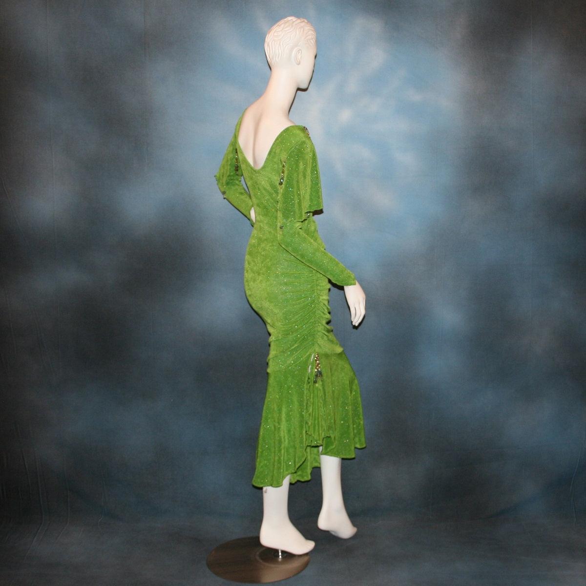 side view of Apple green social Latin/rhythm dress was created of apple green glitter slinky, features ruching on the right side, long sleeves, scoop back, & full skirting with open side that has Swarovski hand beaded detail