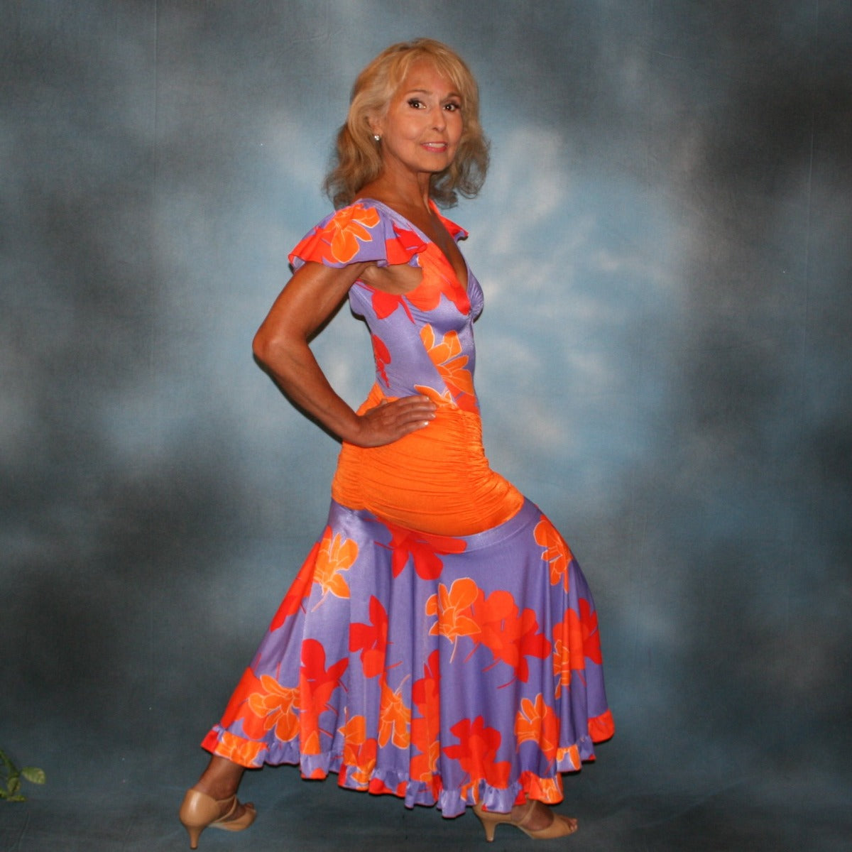 Tropical print social ballroom dress created in lycra of deep orchid tropical print with purple flowers, features ruffly cap sleeves & ruffle on full circle skirt. The bodysuit is built right into the dress, so it makes a great & fun dress for teaching, especially if you work on theater arts! The look is finished with an orange ruched hip sash.