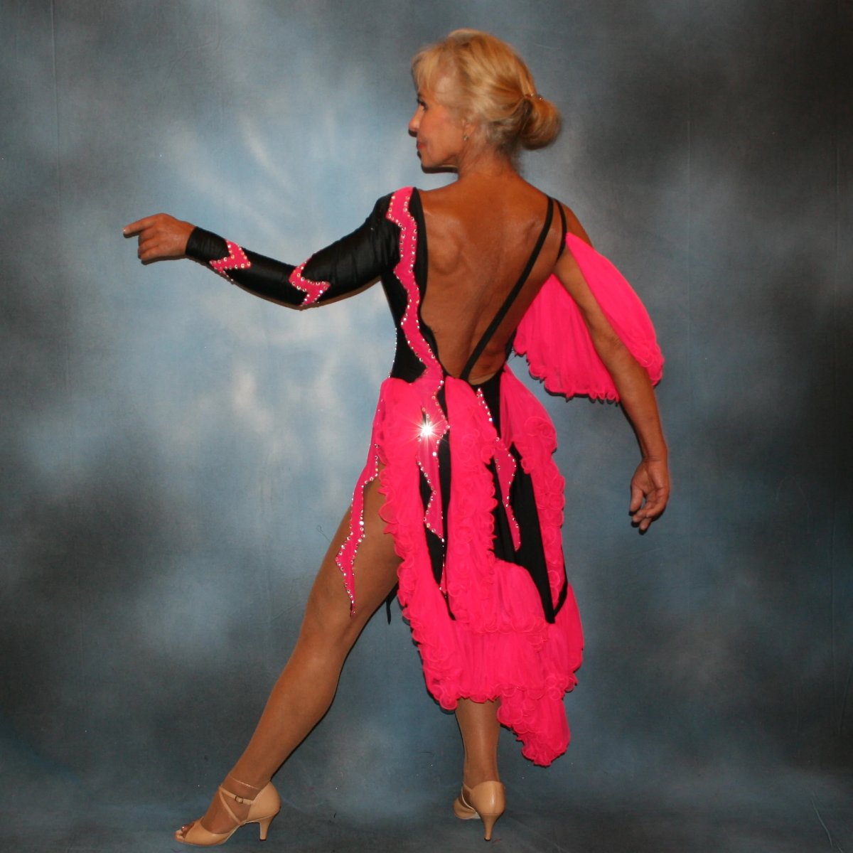 side back view of Black Latin/rhythm dance dress with hot pink accents created in black lycra with hot pink hand cut zig zag artwork appliqued detail work & ruffles of hot pink sheer tricot, is embellished with crystal Swarovski rhinestone work.