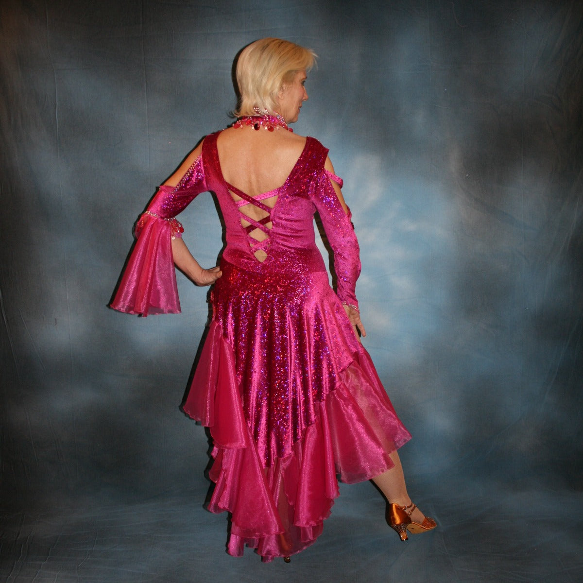  back view of Crystal's Creations Fuchsia Latin/rhythm dress created of fuchsia glitter stretch velvet with fuchsia organza flounces, lattice detail strap work on one long sleeve, embellished with detailed Swarovski rhinestone work, along with hand beading & spangles on sale! A matching neckpiece is included.