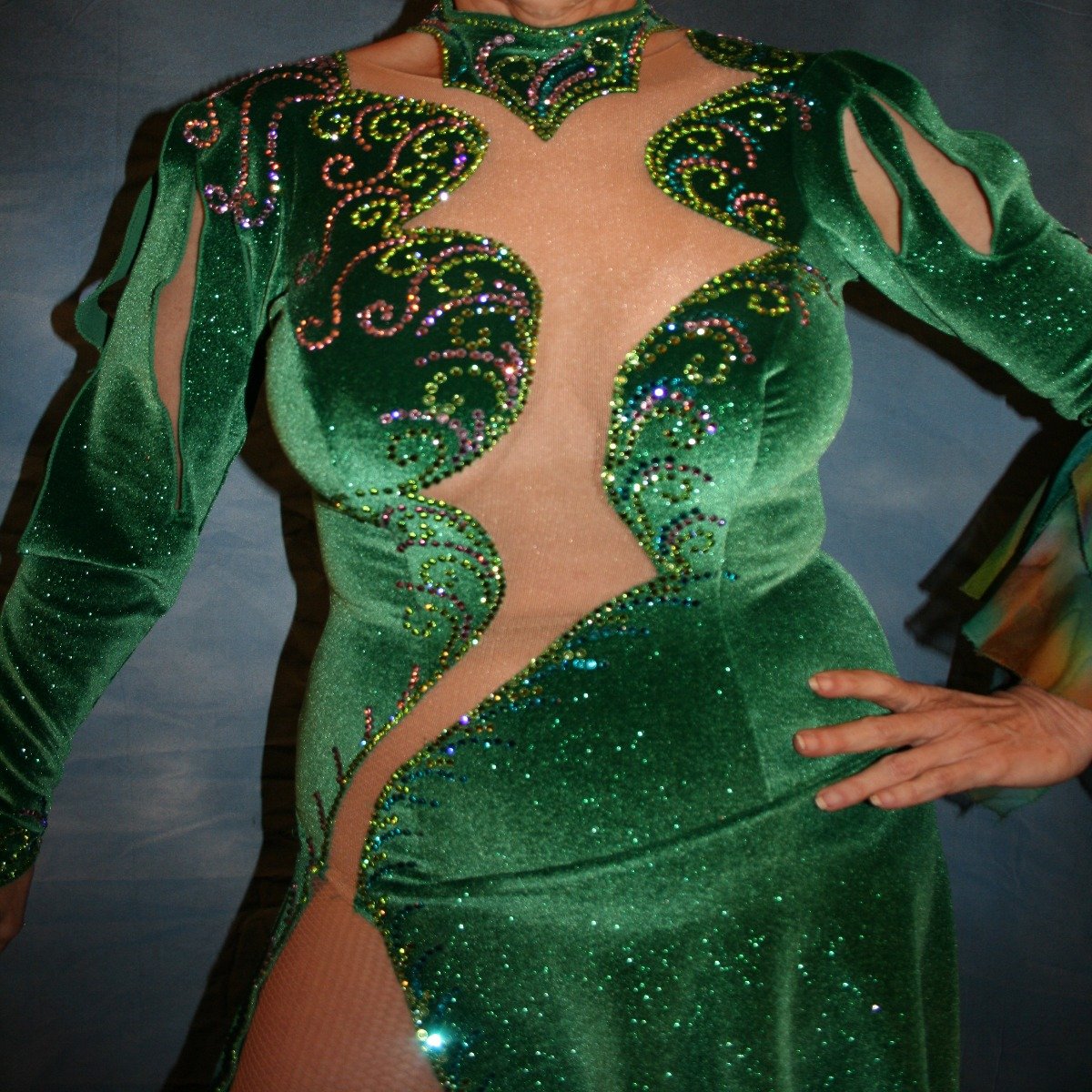 close upper view of Green Latin/rhythm dress was created in luxurious deep emerald green glitter stretch velvet with accent flounces of a green print chiffon. It features nude illusion cutout through the bodice, & is embellished with detailed Swarovski rhinestone work of peridot, emerald & orchid.