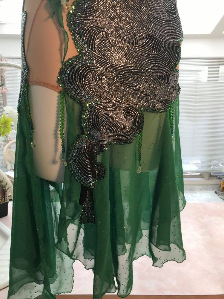 Crystal's Creations close bottom view of silver Latin/rhythm dress with emerald green accents created of intricately cut & artistically placed silver swirls glitter slinky on a nude illusion base, with skirting & accent pieces of an emerald green size 5/6-9/10