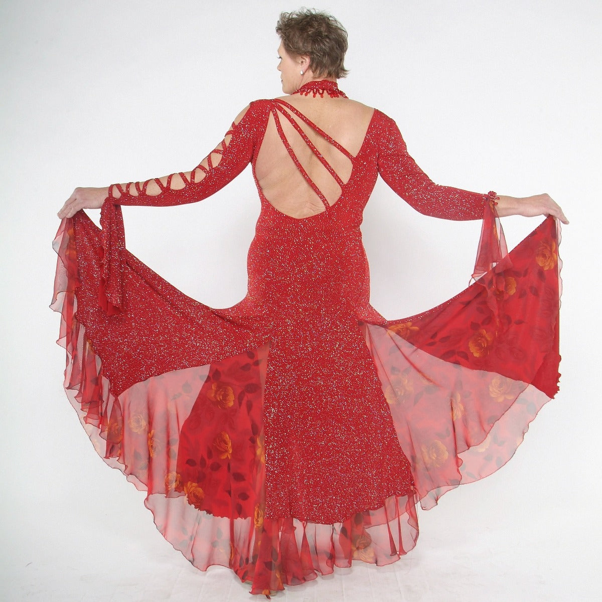back view of Red ballroom dress created in red glitter slinky with print chiffon insets features lattice detailing in bodice along with matching hand beaded choker…hand beading at the edge of right sleeve.