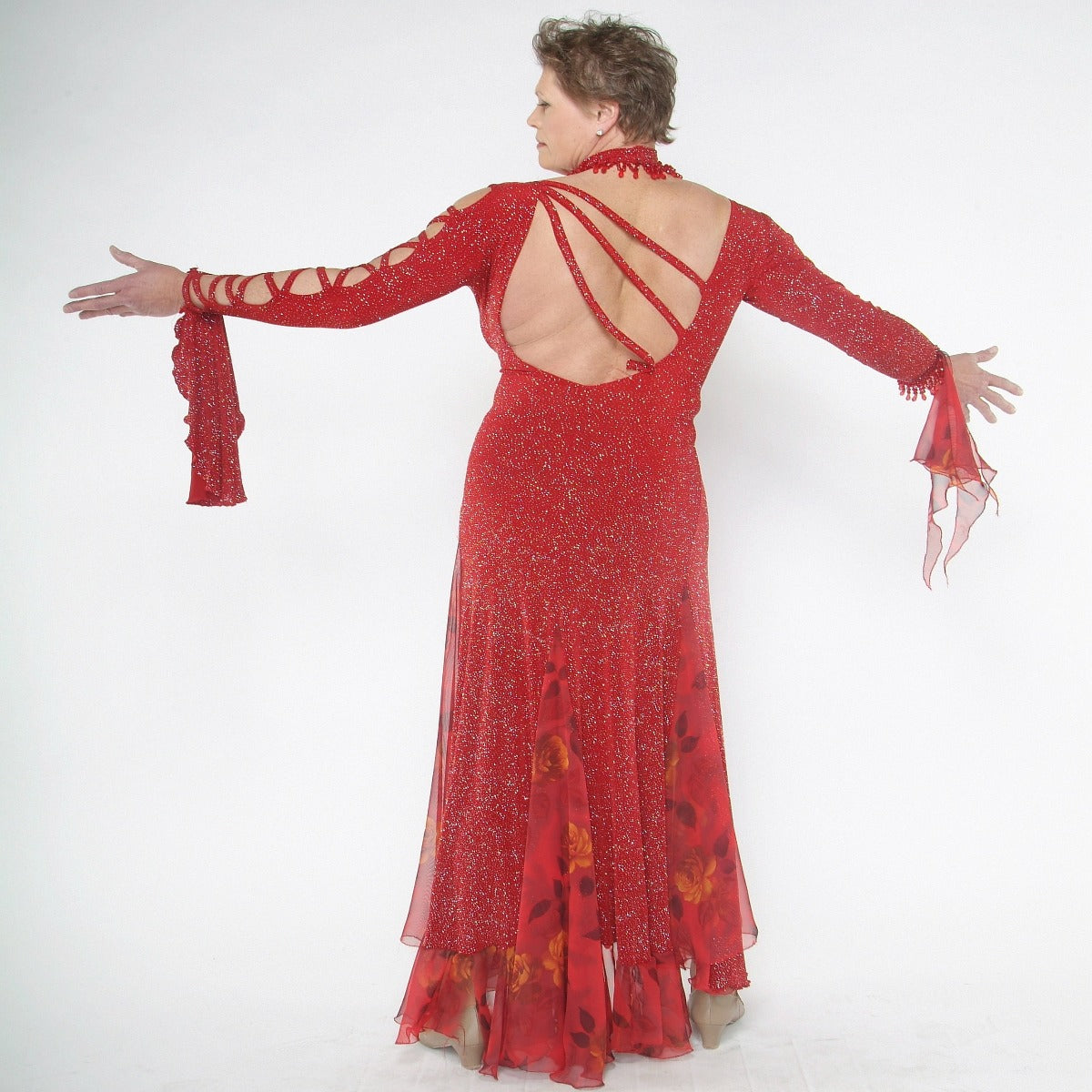 back view of Red ballroom dress created in red glitter slinky with print chiffon insets features lattice detailing in bodice along with matching hand beaded choker…hand beading at the edge of right sleeve.